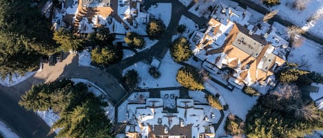 Vista aérea de una zona residencial con varias casas, rodeadas de árboles y cubiertas de nieve.
