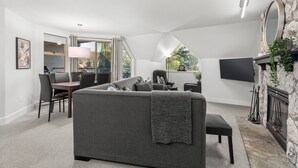 A modern living room with a grey sofa, dining area, stone fireplace, and a TV mounted on the wall.