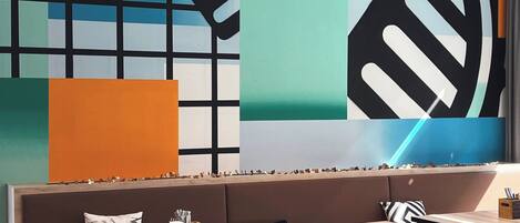 A modern interior with a long bench seating area, wooden tables, and a large abstract wall mural.