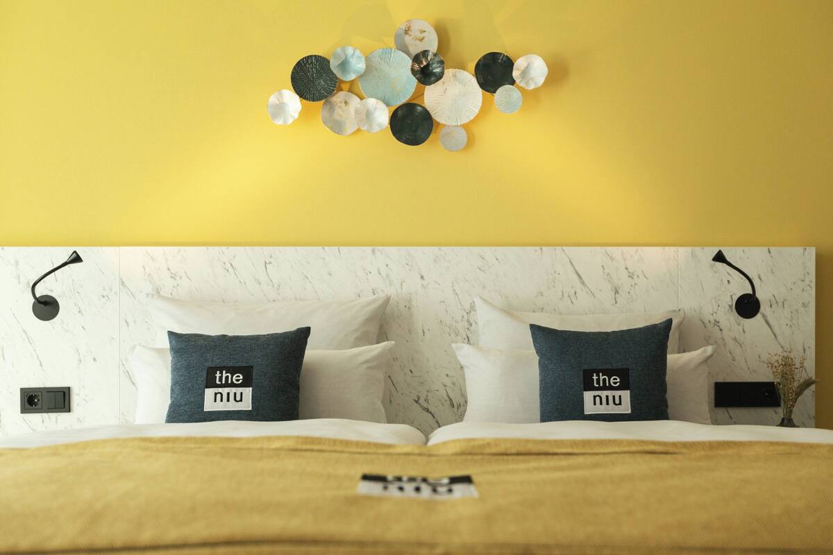 Una cama con dos almohadas, un aplique de pared y una obra de arte decorativa.