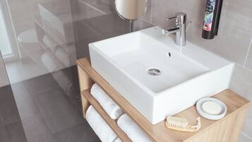 A modern bathroom with a white sink, a wooden vanity, a round mirror, a soap dispenser, and a towel rack.