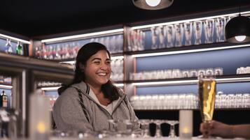 A bar area with shelves of glasses and bottles, a person holding a glass, and a bar counter.