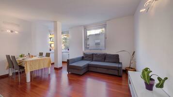 A modern living room with a dining area, a grey sectional sofa, a small table with a plant, and a window with a view.