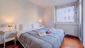 A bedroom with a bed, bedside tables, a window, and a view of buildings. - Sunlight - 150m From the Lake (Lugano)
