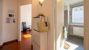 A hallway with a chair, a basket, a radiator, and a window with a view of buildings. - Sunlight - 150m From the Lake (Lugano)