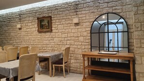 A dining area with a stone wall, wooden chairs, a table with a white tablecloth, and a wooden sideboard. - Port Royal Hotel (Paris)