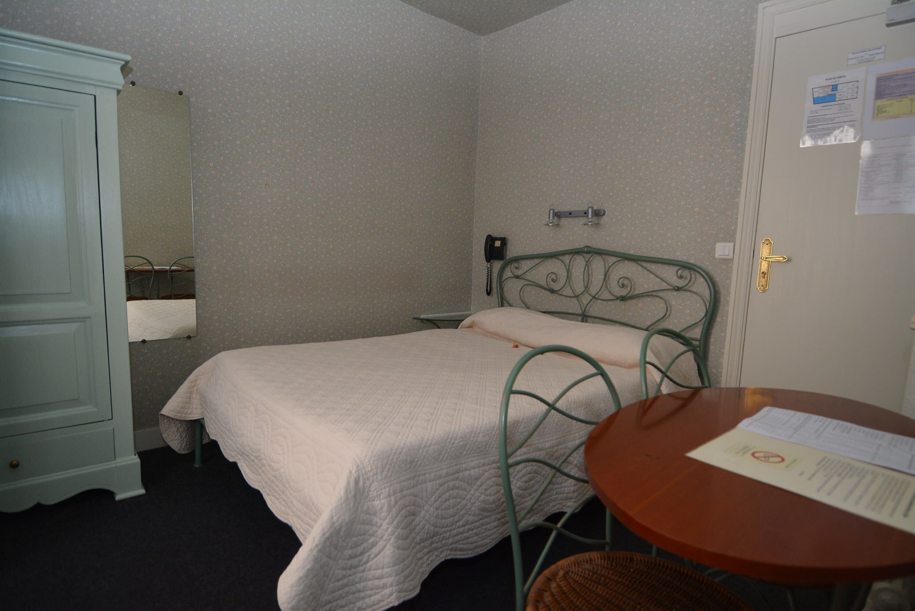 A small, neatly arranged bedroom with a single bed, a chair, a table, and a wardrobe.