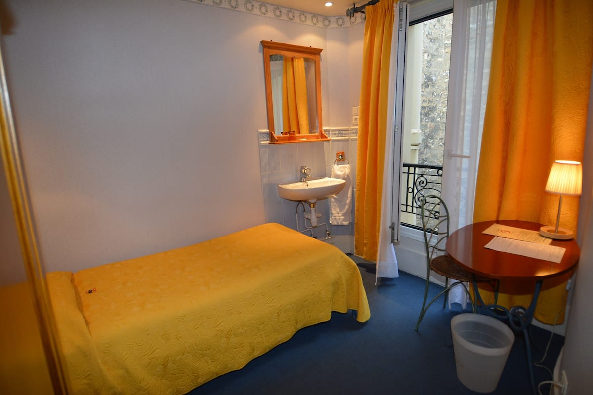 A small room with a bed, a sink, a chair, a table, and a view of the outside.