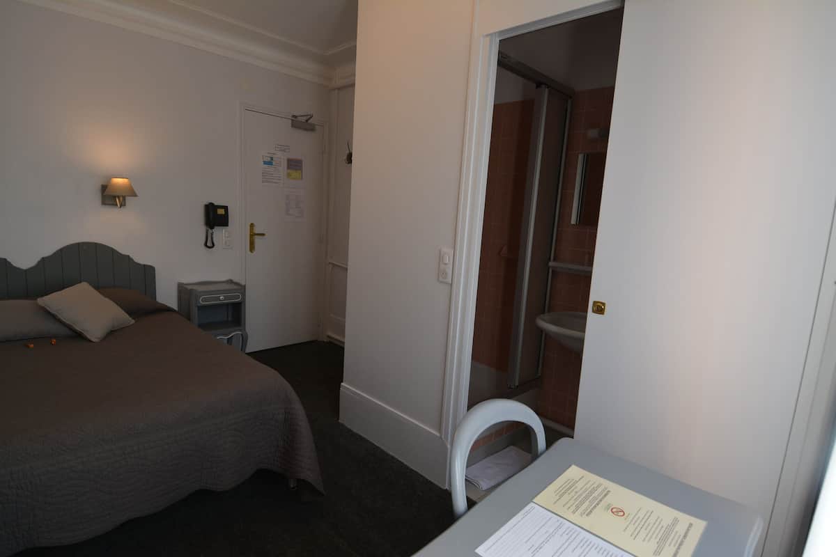 A hotel room with a bed, bedside table, lamp, and a bathroom visible through an open door.