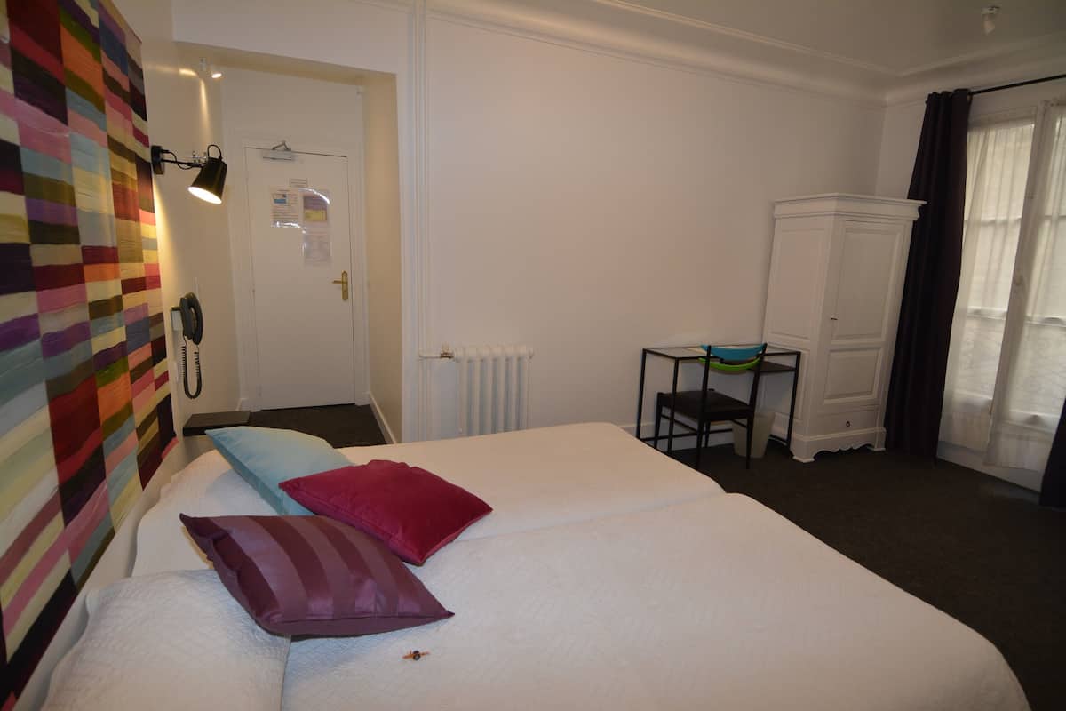 A hotel room with a bed, a chair, a radiator, a cabinet, and a door with a notice.