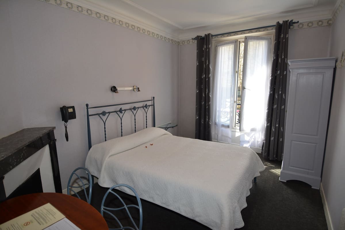 A bedroom with a single bed, a bedside table, a chair, a wardrobe, and a window with curtains.