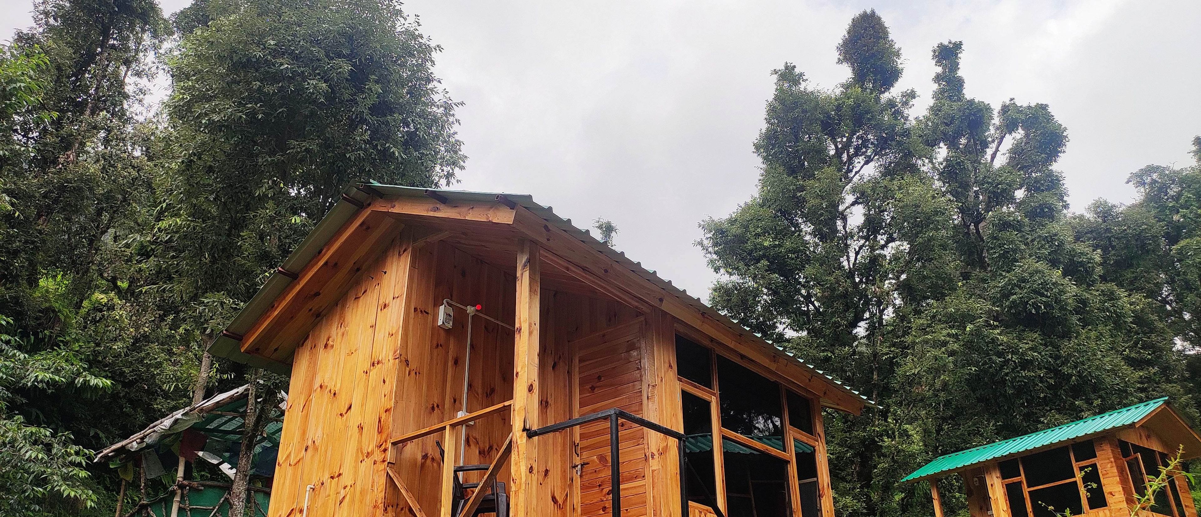 A wooden cabin with a balcony, surrounded by dense forest.