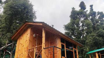 A wooden cabin with a balcony, surrounded by dense forest.