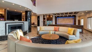 A modern hotel lobby with a curved seating area, a fireplace, a large flat-screen TV, and a bar area with a blue-lit wall. - Best Western Premier Liberty Inn & Suites (Liberty)