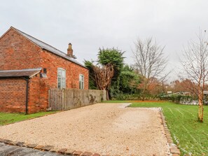 A gravel driveway leading to a brick house with a wooden fence and a large tree in the background. - Mill Lane Cottage (Chester)