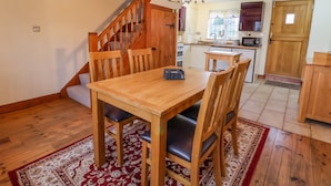 Un coin repas avec une table et des chaises en bois, un tapis rouge à motifs et un escalier menant à une autre pièce.