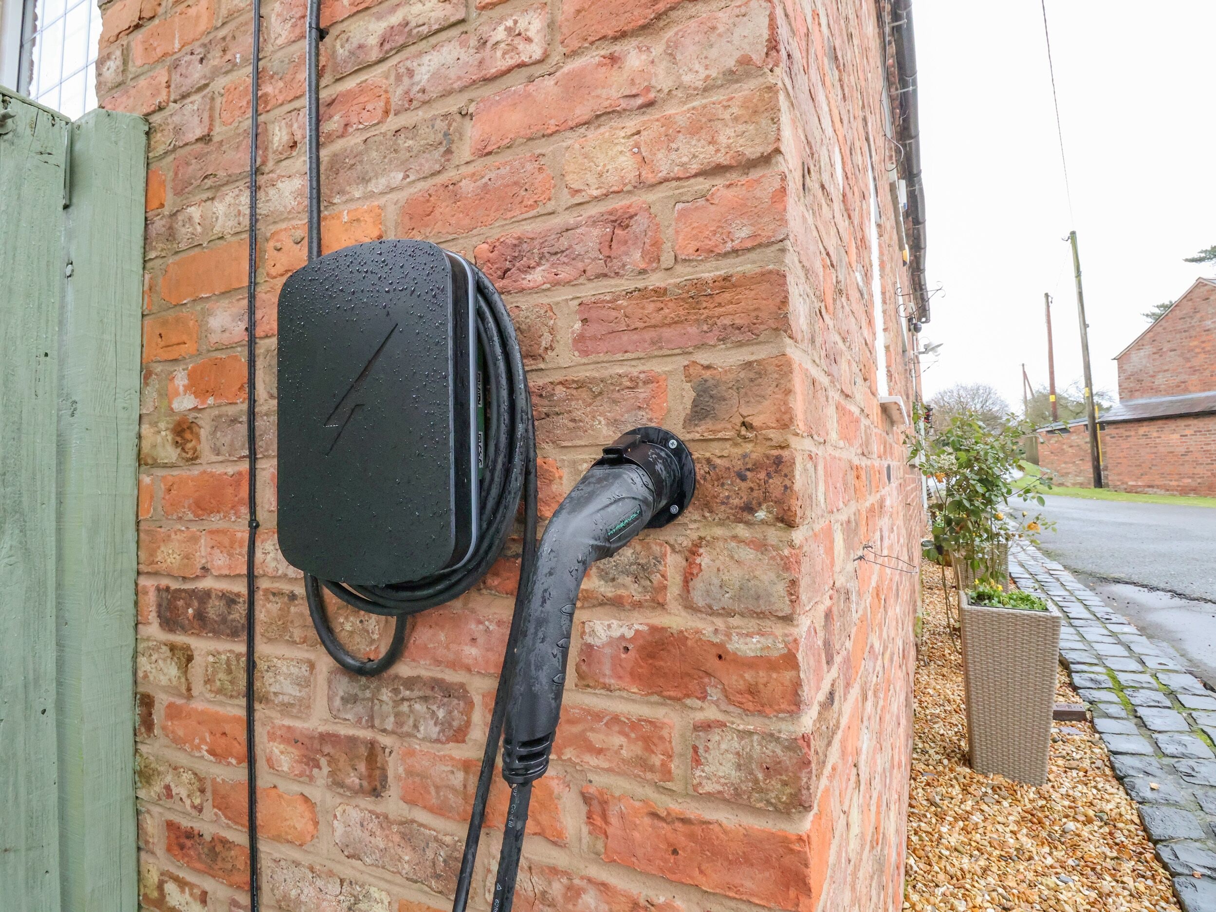 A brick wall with a black electrical box and a cable plugged into it.