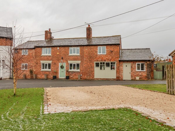 A two-story brick house with a green door, a small attached garage, and a gravel driveway. - Mill Lane Cottage (Chester)
