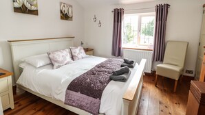 Une chambre à coucher bien rangée, avec un lit en bois, une table de chevet, une chaise et une fenêtre avec des rideaux.