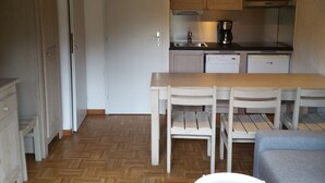 Pieni, käytännöllinen keittiö, jossa on valkoiset kaapit, puinen pöytä ja kaksi tuolia.