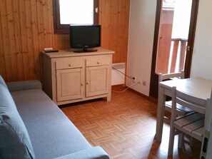 Een kamer met een houten vloer, een grijze bank, een klein wit tafeltje en een televisie op een houten kast.