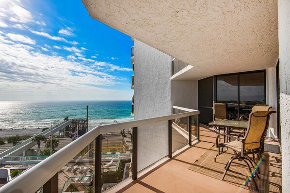 Un balcon avec vue sur l’océan, un coin repas avec des chaises et une table, et un bâtiment à la façade texturée.
