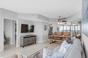 A spacious living room with a large flat-screen TV, a wooden dining table, and a comfortable sofa.