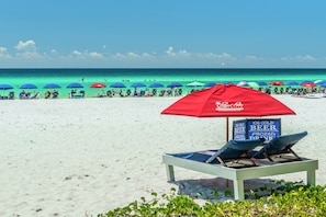 A beach with lounge chairs and umbrellas, a sign advertising ice cold beer and frozen drinks, and the ocean in the background.