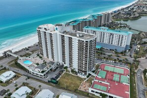 Un hôtel de grande hauteur, avec de nombreux étages, une piscine, des courts de tennis et une vue sur la plage.