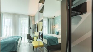 A hotel room with two beds, a desk, and a chair. There is a mirror on one wall and a lamp on the desk. - Holiday Inn - the niu, Seven Dusseldorf Ost by IHG (Düsseldorf)