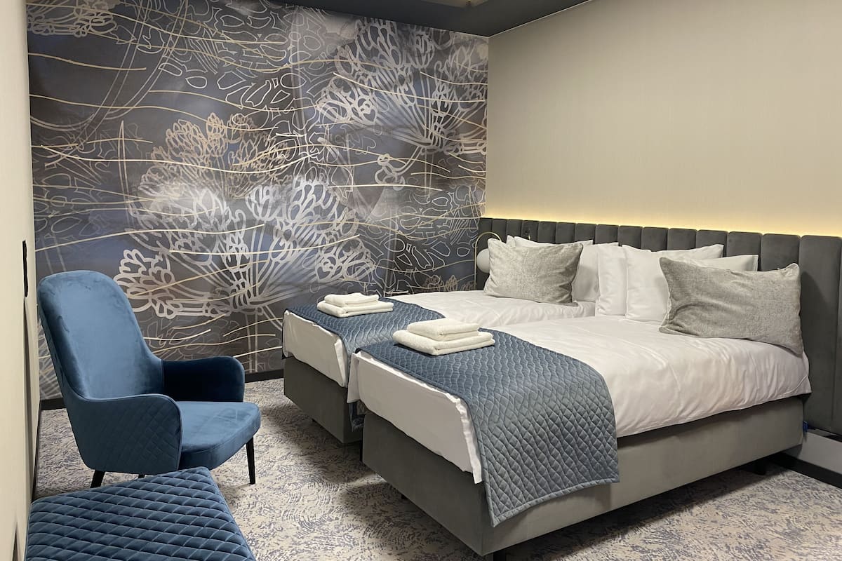 Un dormitorio moderno con una cama grande, dos mesitas de noche, un sillón azul y un adorno en la pared.