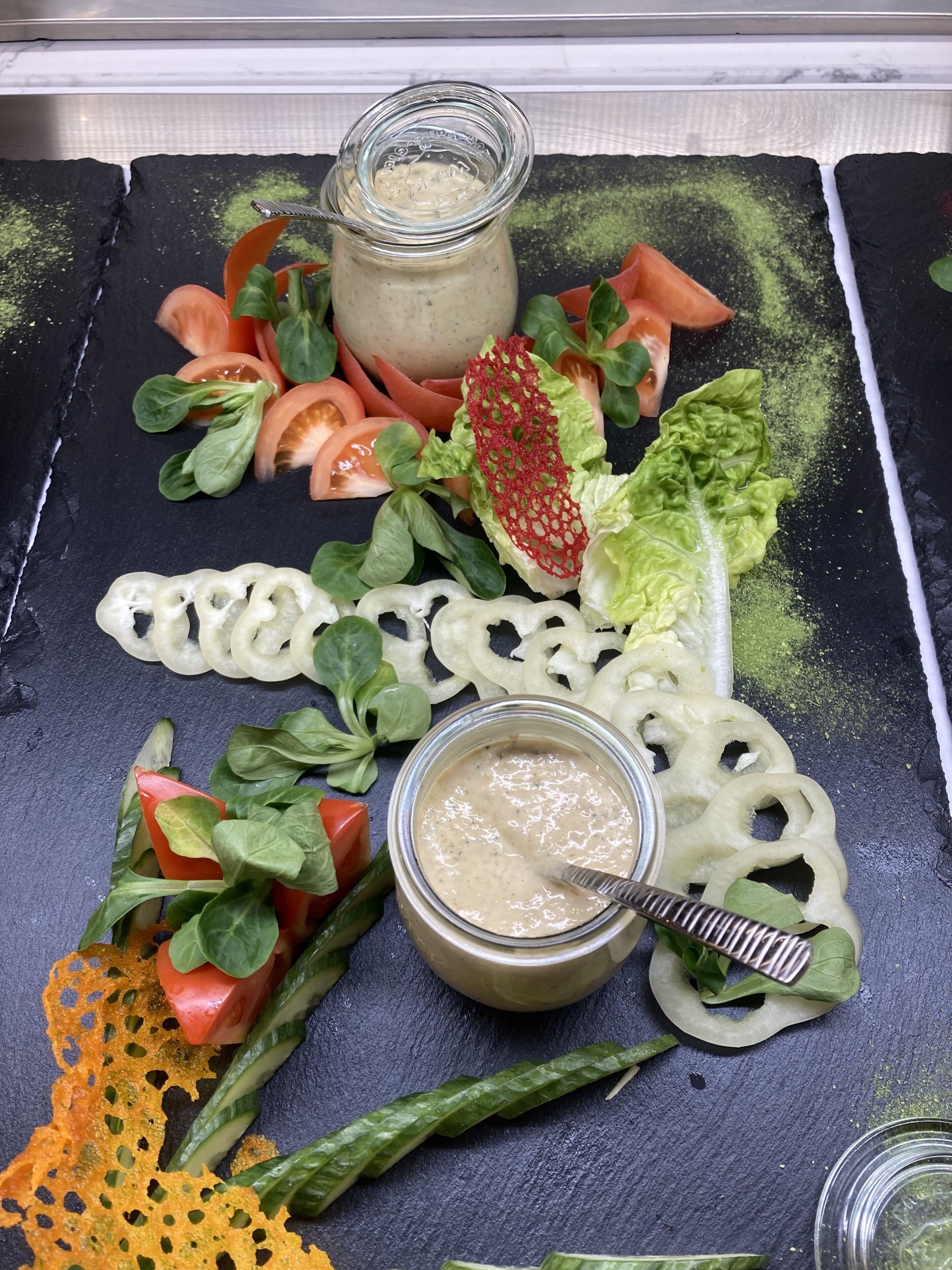 A salad with various vegetables and a jar of dressing on a slate board.