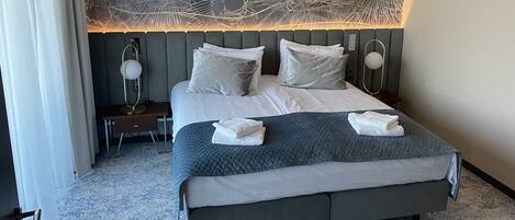 A modern hotel room with a large bed, grey bedding, and a decorative wall mural.