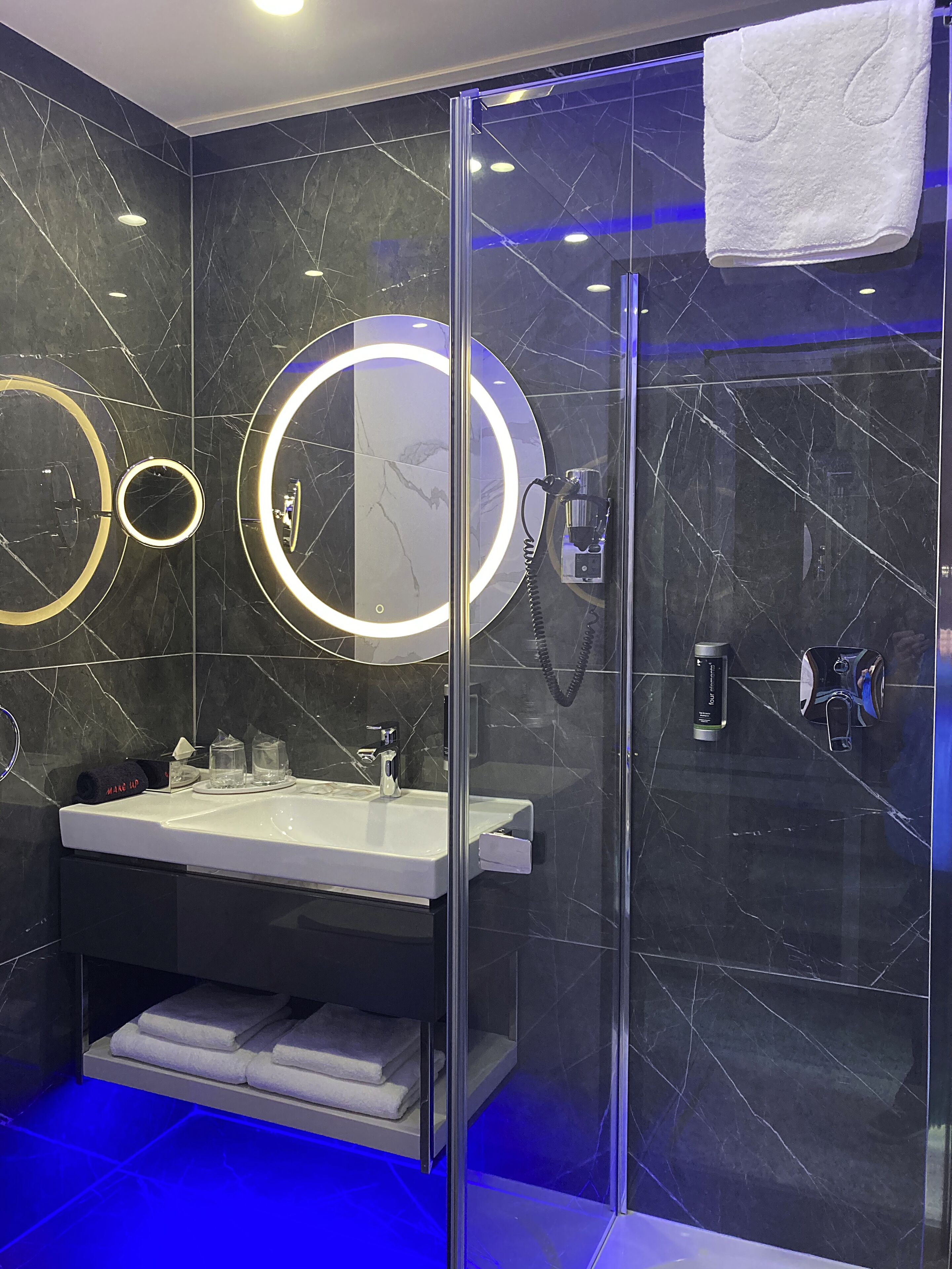 A modern bathroom with a glass-enclosed shower, a vanity with a sink, and two illuminated mirrors.