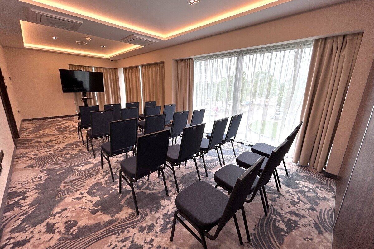 A conference room with rows of chairs, a large flat-screen TV, and a patterned carpet.