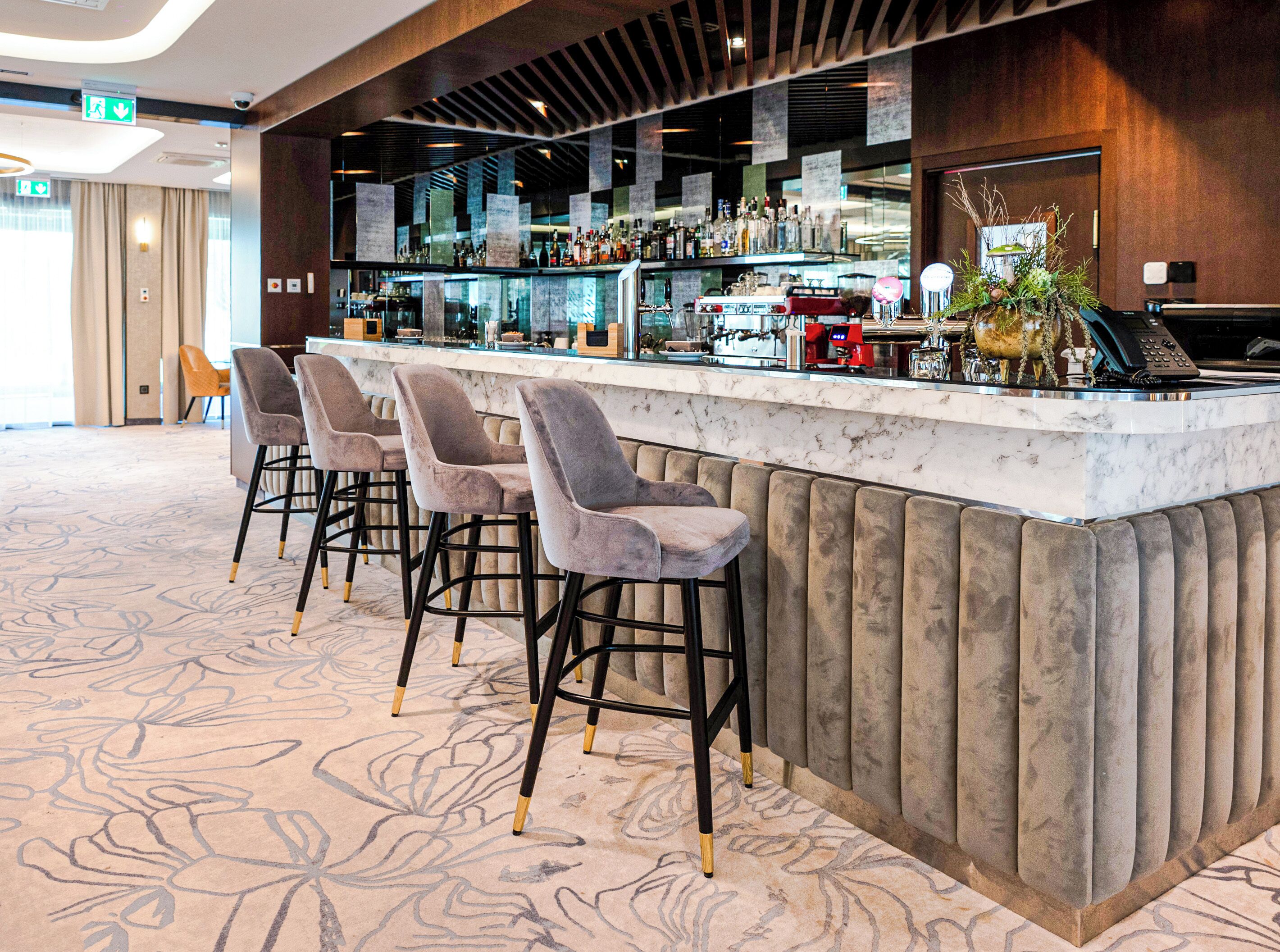 A bar area with a marble countertop, three cushioned bar stools, and a variety of bottles and glasses.