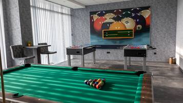 A pool table with a green felt surface and a cue ball, a foosball table, and a billiards table with a colorful ball arrangement.