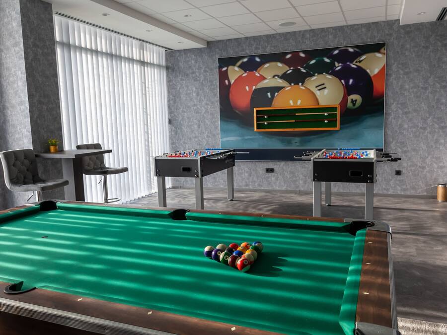 A pool table with a green felt surface and a cue ball, a foosball table, and a billiards table with a colorful ball arrangement.