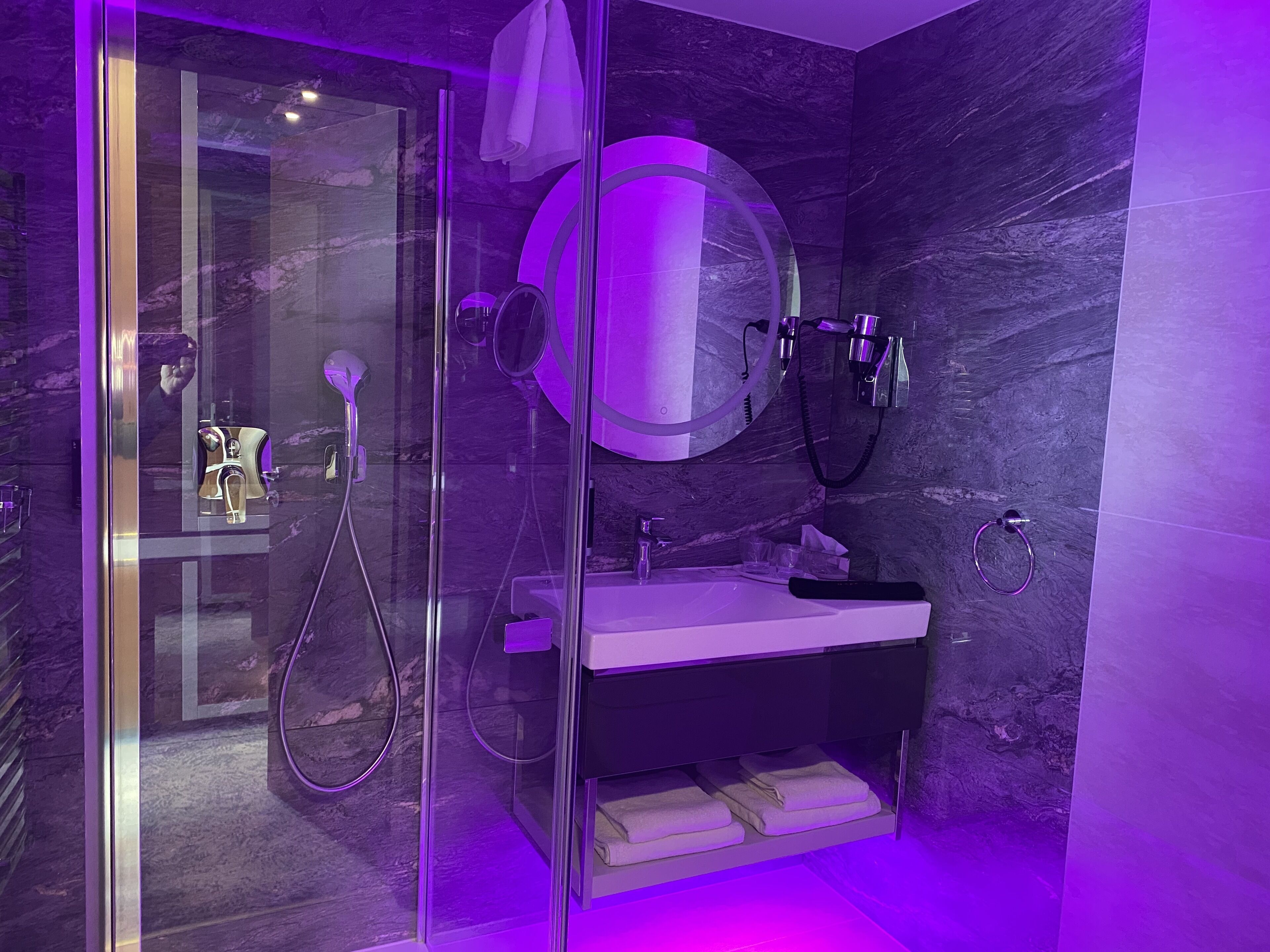 Un baño moderno con ducha envuelta en vidrio, tocador con lavamanos y un espejo grande.
