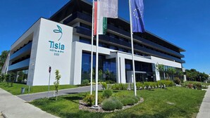 Edificio moderno del hotel Tisia & Spa con fachada de vidrio, varios balcones y un jardín ajardinado.