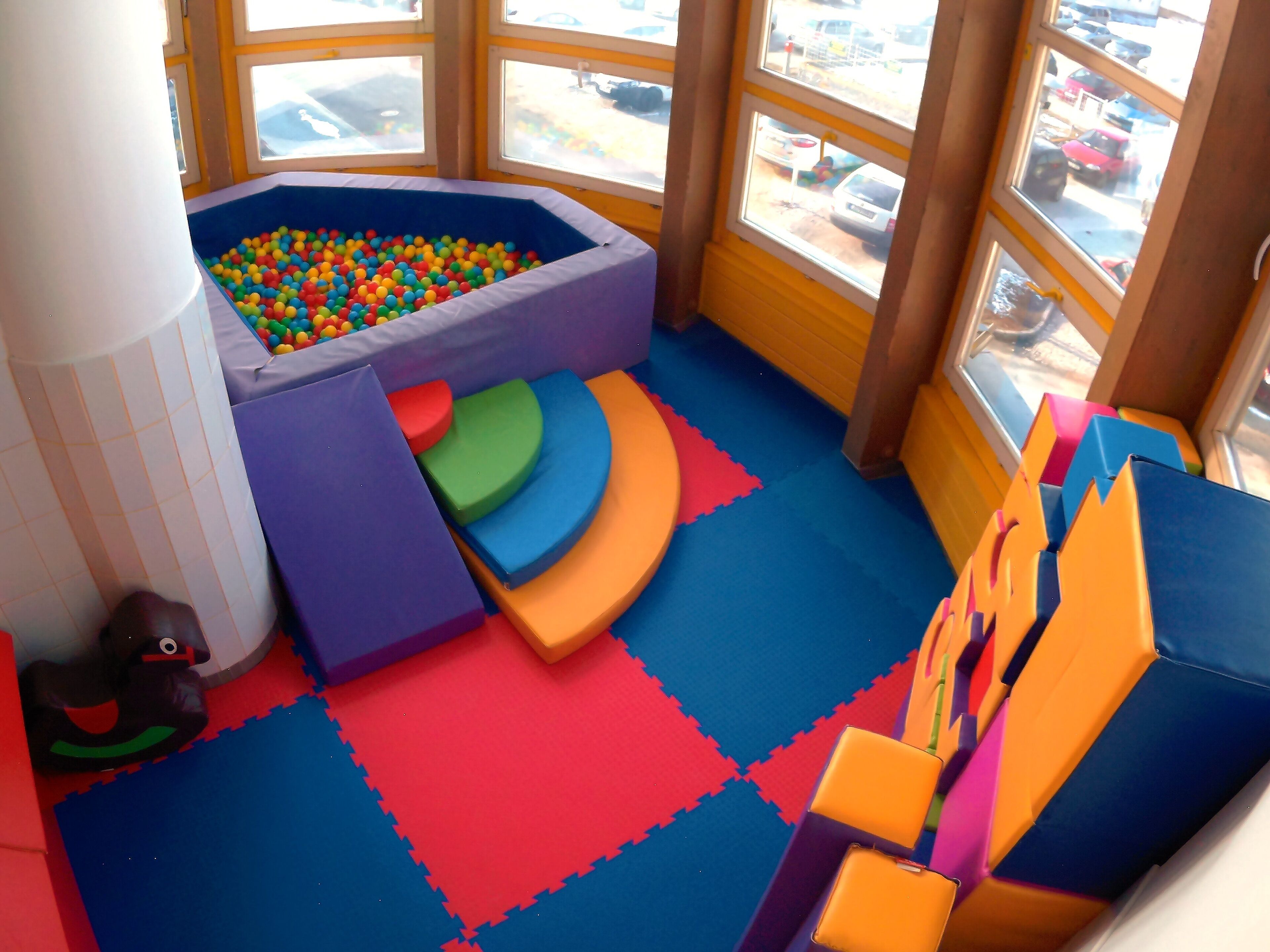 A play area with a ball pit, padded seating, and a window view.