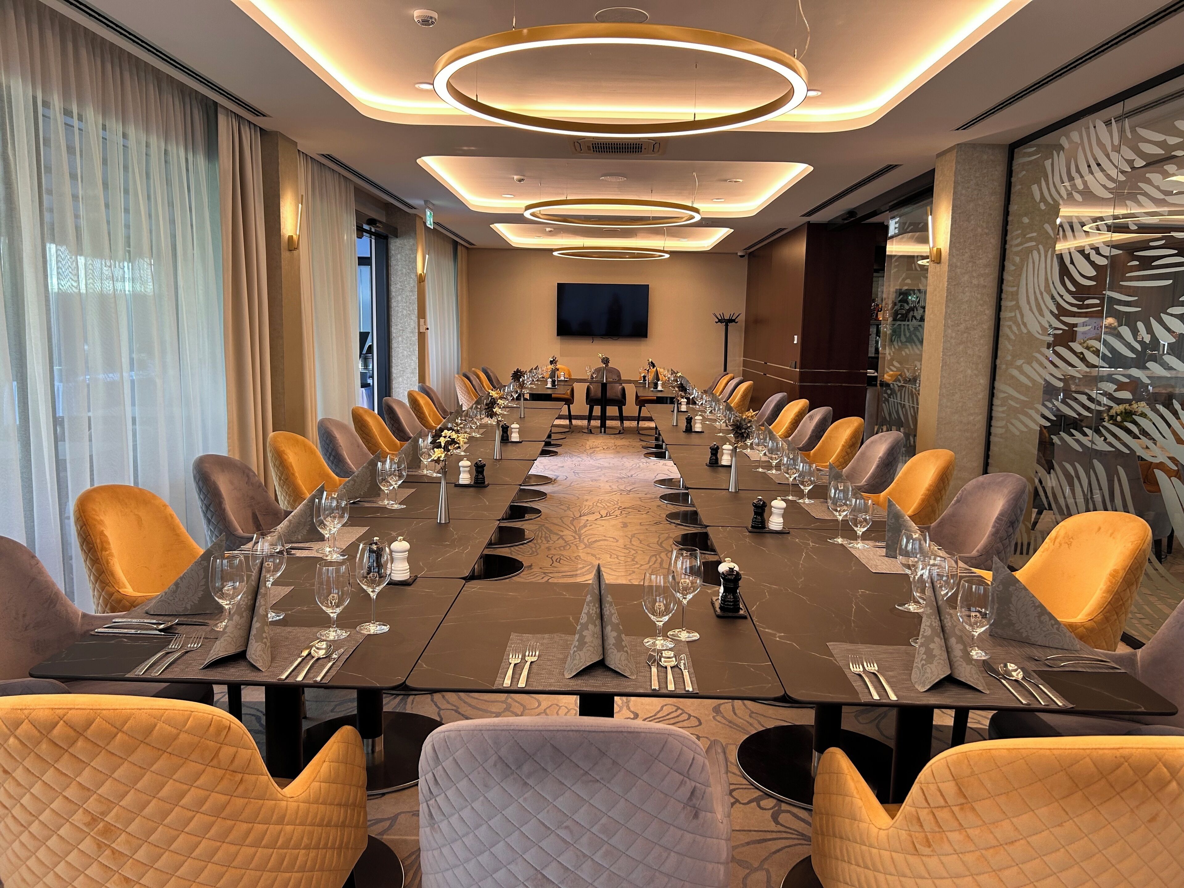 Ein Konferenzraum mit einem langen Tisch, gedeckt für ein Meeting, umgeben von Stühlen und modernen Leuchten an der Decke.