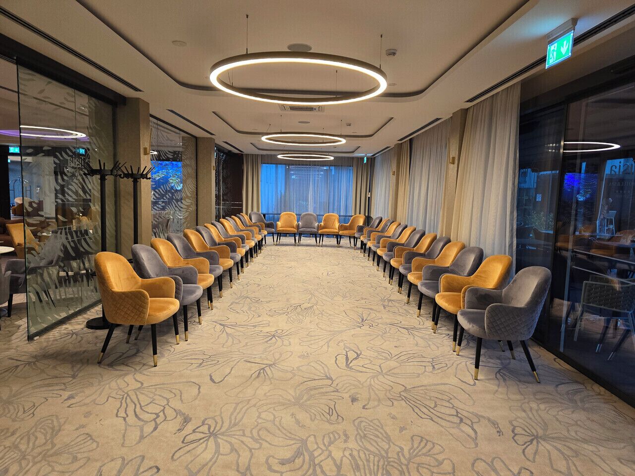 A conference room with a long table and rows of chairs, large windows, and a patterned carpet.
