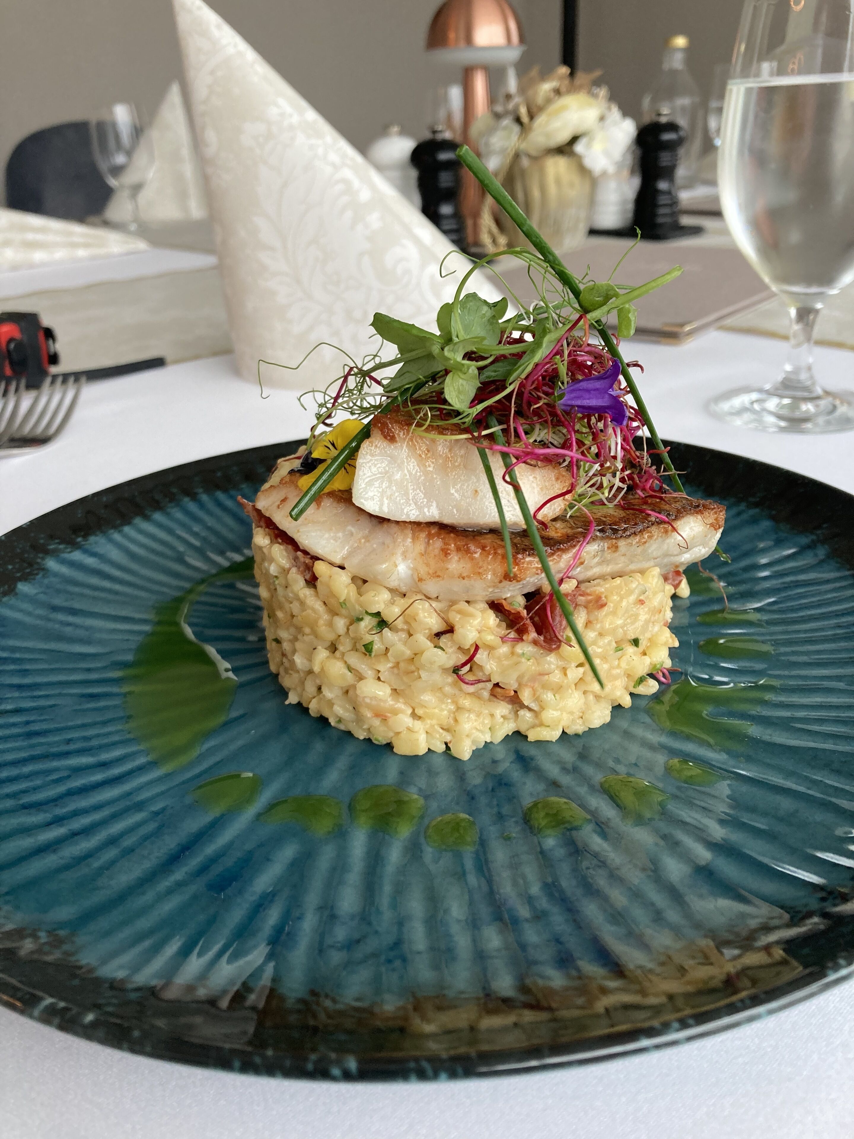 A plate of food with a piece of fish and rice, garnished with greens and purple flowers.