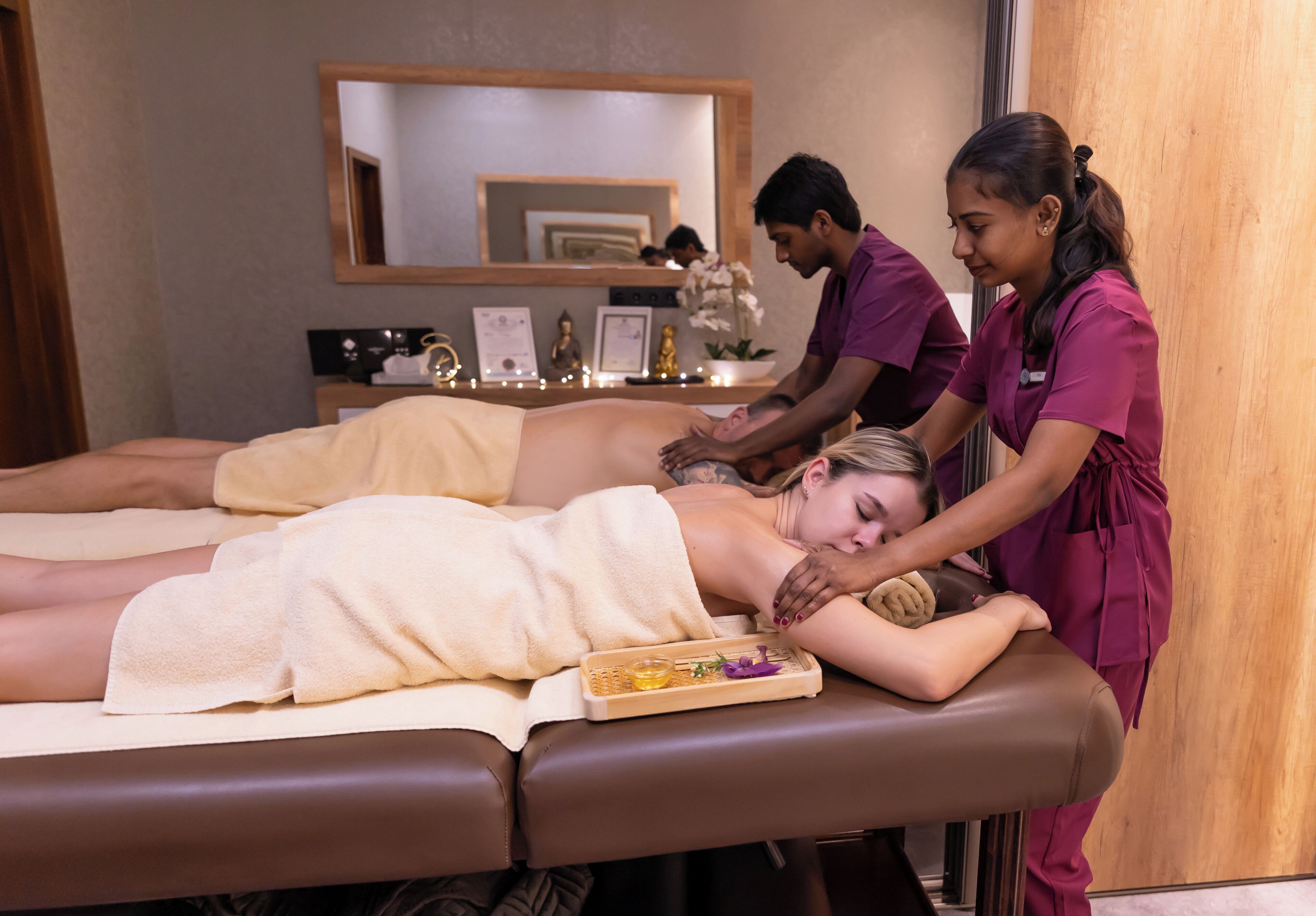 A massage therapy room with two massage tables, a wooden cabinet, and a mirror on the wall.
