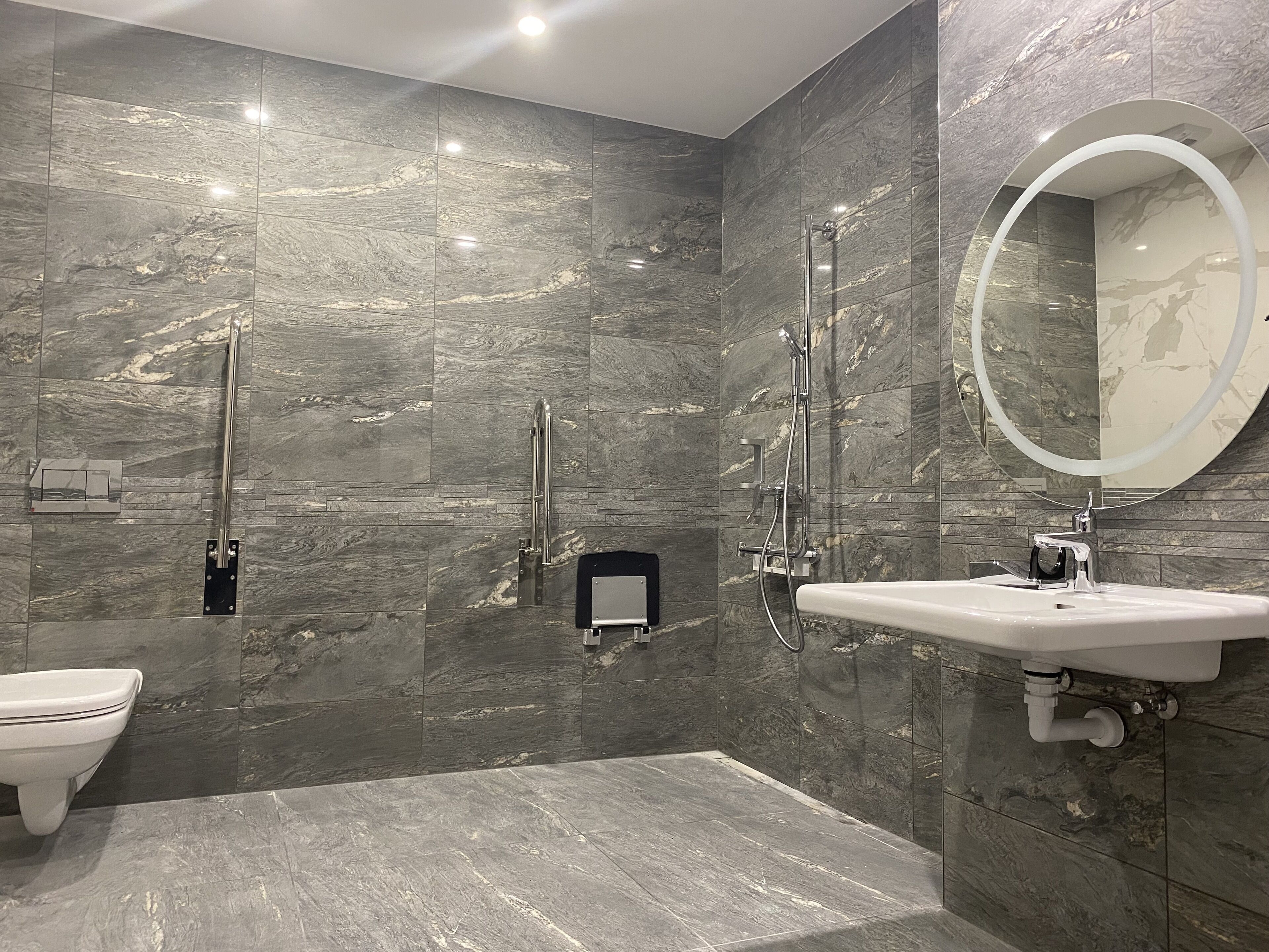Un baño moderno con salpicadero de mármol, un espejo redondo, un inodoro y una zona de ducha.