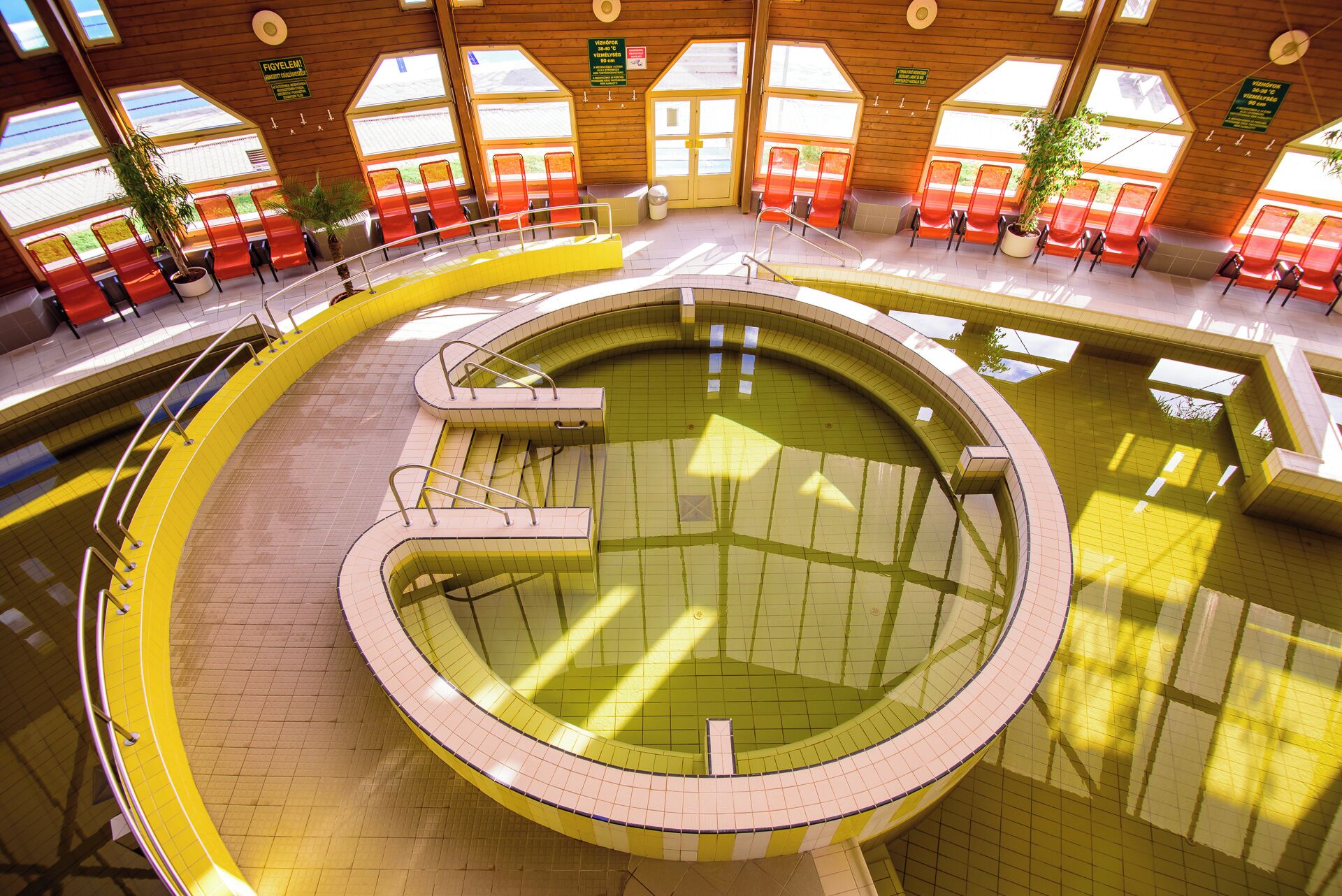 A large indoor swimming pool with multiple lanes, surrounded by seating areas and large windows.