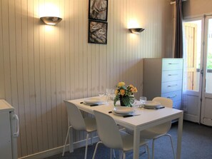 A dining area with a white table set for two, two chairs, a vase of yellow flowers, and two wall-mounted lights.