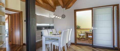 A modern kitchen with white cabinets, a dining area with a white table and chairs, and a wooden ceiling.