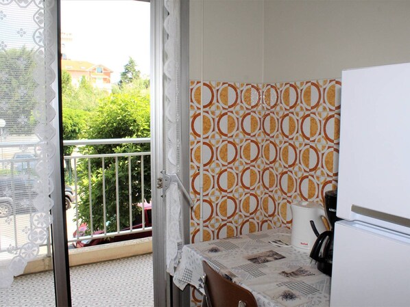 A small kitchen with a refrigerator, a table with a tablecloth, and a patterned wall.